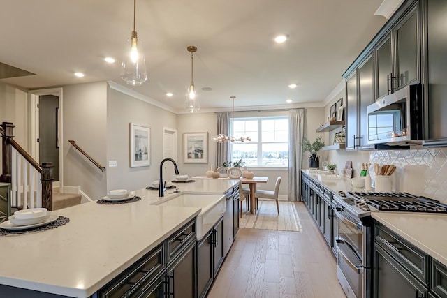 kitchen with sink, crown molding, hanging light fixtures, a center island with sink, and appliances with stainless steel finishes