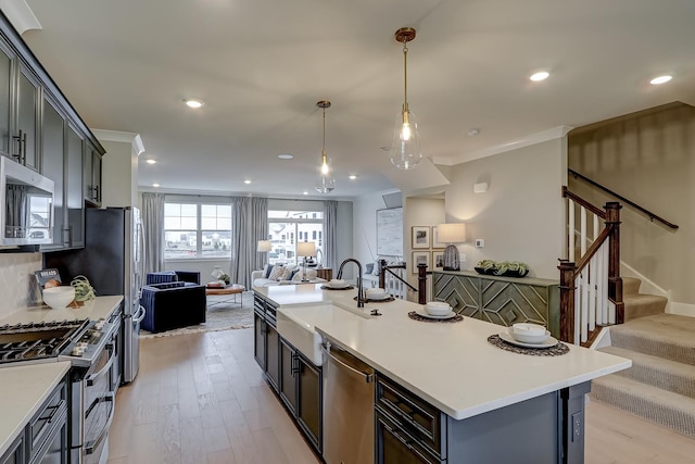 kitchen with pendant lighting, sink, light hardwood / wood-style flooring, appliances with stainless steel finishes, and a kitchen island with sink