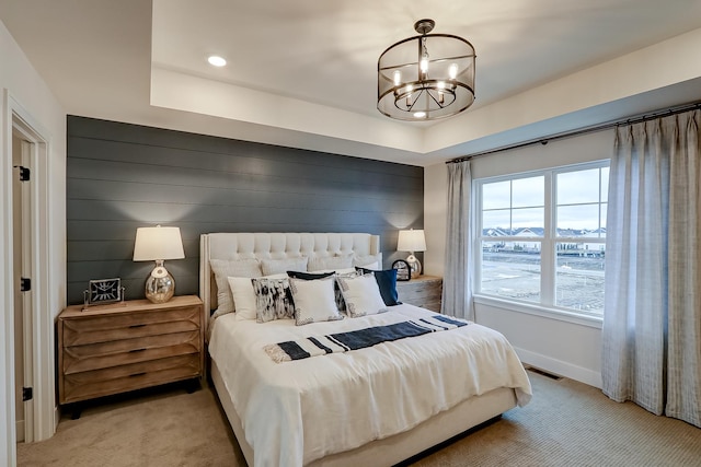 carpeted bedroom featuring a tray ceiling, a chandelier, and wood walls