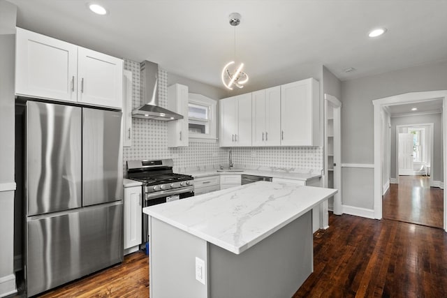 kitchen with white cabinetry, sink, a center island, stainless steel appliances, and wall chimney range hood