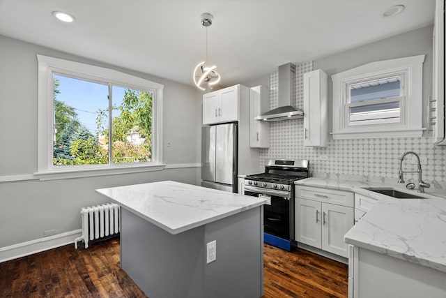 kitchen featuring sink, hanging light fixtures, radiator heating unit, stainless steel appliances, and wall chimney range hood