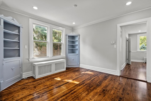 empty room featuring crown molding, plenty of natural light, radiator, and dark wood-type flooring