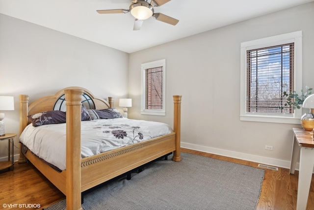 bedroom featuring a ceiling fan, visible vents, baseboards, and wood finished floors