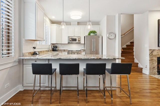 kitchen featuring a peninsula, wood finished floors, white cabinetry, appliances with stainless steel finishes, and decorative backsplash