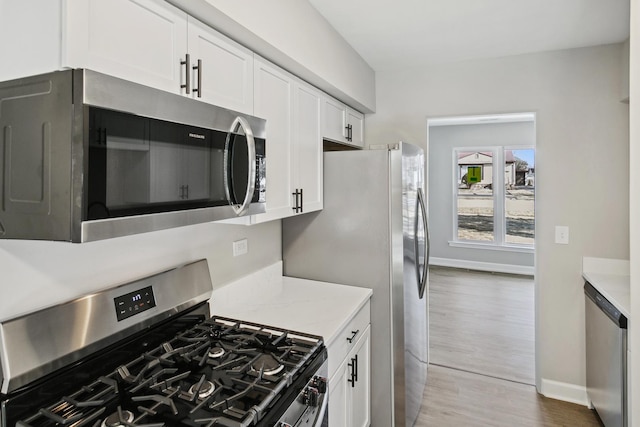 kitchen with white cabinetry, light stone counters, light hardwood / wood-style floors, and appliances with stainless steel finishes