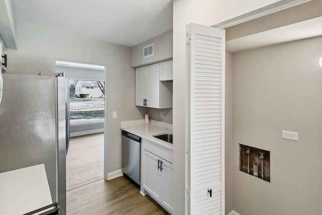 kitchen with appliances with stainless steel finishes, hardwood / wood-style floors, and white cabinets