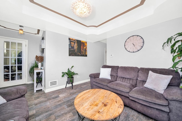 living room featuring dark wood-type flooring, a tray ceiling, and a chandelier