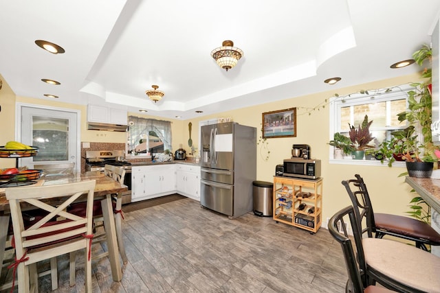 kitchen featuring light hardwood / wood-style flooring, a raised ceiling, white cabinets, and appliances with stainless steel finishes