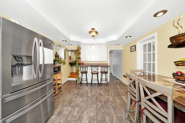 kitchen featuring a breakfast bar, wood-type flooring, white cabinets, a tray ceiling, and stainless steel appliances