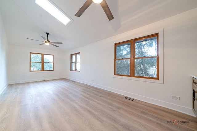 unfurnished room with ceiling fan, vaulted ceiling with skylight, and light hardwood / wood-style floors