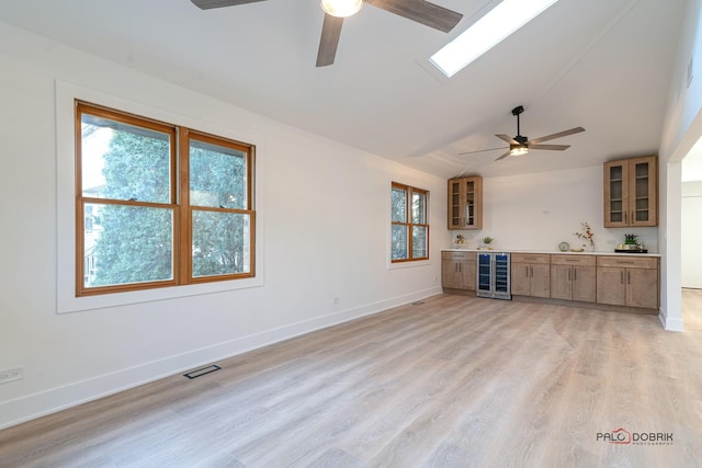 unfurnished living room featuring wine cooler, bar area, vaulted ceiling, ceiling fan, and light hardwood / wood-style floors