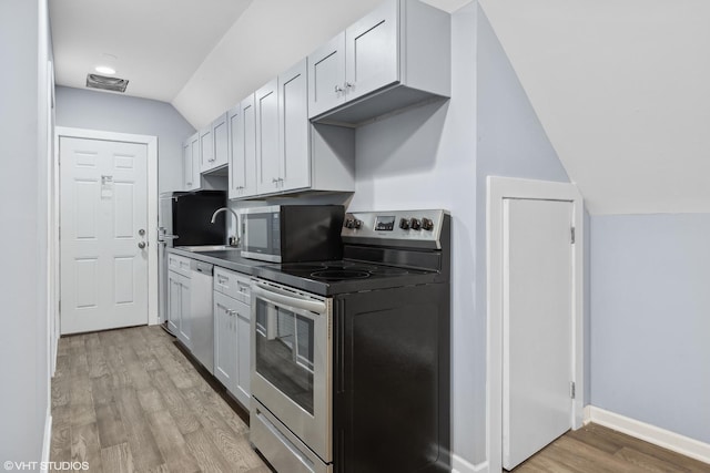 kitchen with vaulted ceiling, sink, white cabinets, stainless steel appliances, and light wood-type flooring