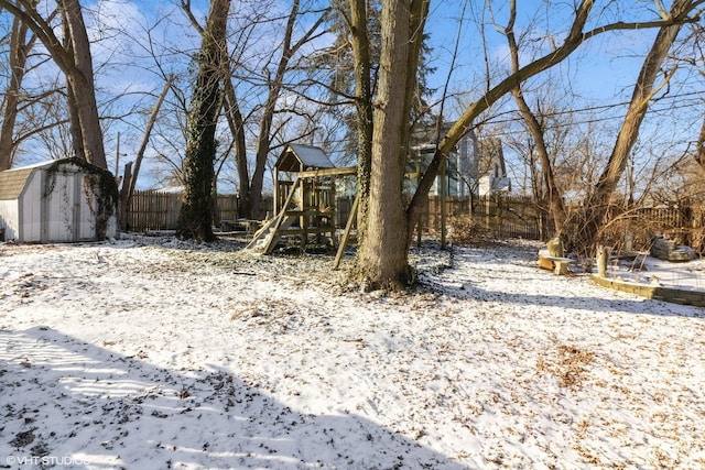 yard layered in snow with a playground and a storage unit