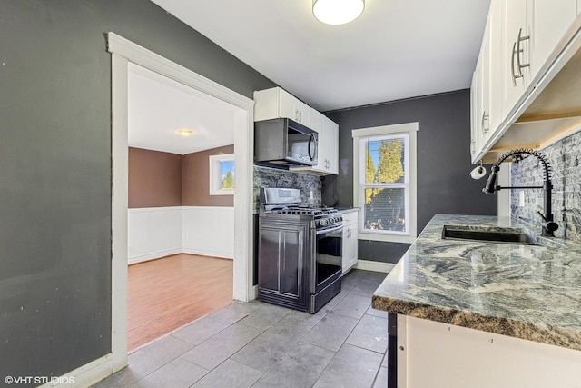 kitchen with stainless steel gas range, sink, light tile patterned floors, dark stone counters, and white cabinets