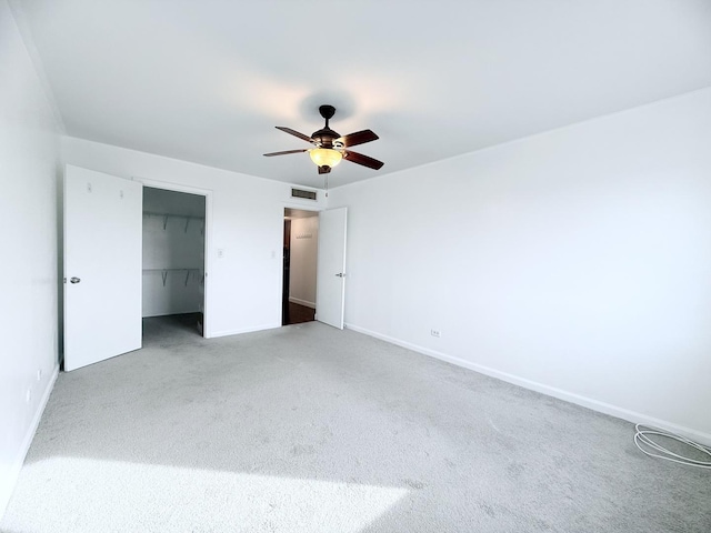 unfurnished bedroom with a walk in closet, carpet floors, a closet, and ceiling fan