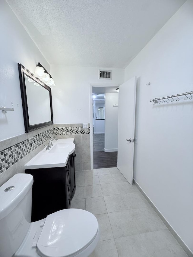 bathroom with tile walls, vanity, a textured ceiling, tile patterned floors, and toilet