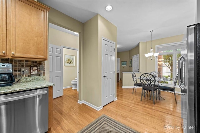 kitchen with light stone counters, decorative light fixtures, light hardwood / wood-style flooring, stainless steel appliances, and decorative backsplash