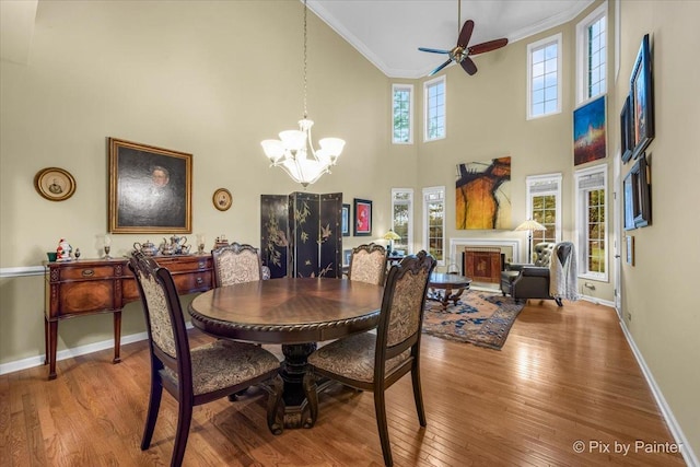 dining area featuring ornamental molding, ceiling fan with notable chandelier, a towering ceiling, and hardwood / wood-style floors