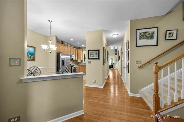 kitchen featuring backsplash, stainless steel appliances, decorative light fixtures, kitchen peninsula, and light wood-type flooring