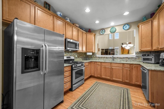 kitchen featuring sink, tasteful backsplash, light wood-type flooring, appliances with stainless steel finishes, and pendant lighting