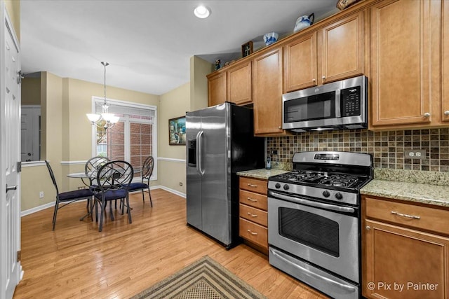 kitchen featuring appliances with stainless steel finishes, hanging light fixtures, light stone countertops, a chandelier, and light wood-type flooring