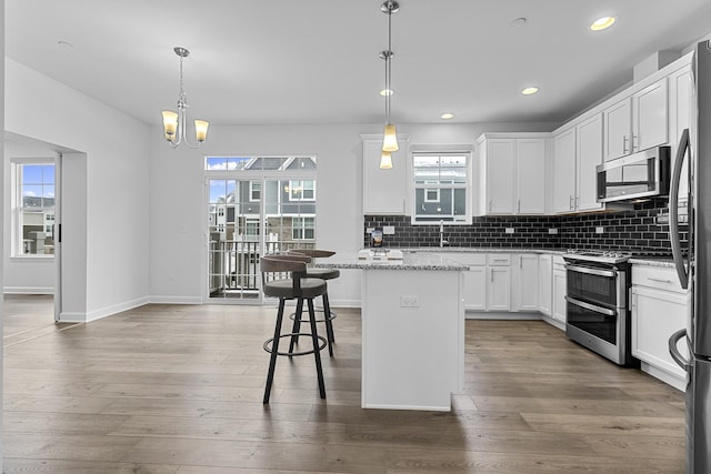 kitchen featuring light stone counters, white cabinetry, hanging light fixtures, appliances with stainless steel finishes, and a kitchen island