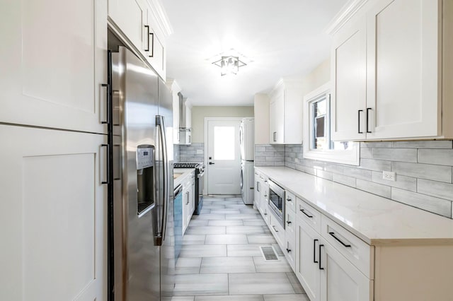 kitchen with backsplash, appliances with stainless steel finishes, light stone countertops, and white cabinets