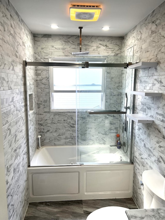 bathroom with hardwood / wood-style floors, shower / bath combination with glass door, and toilet