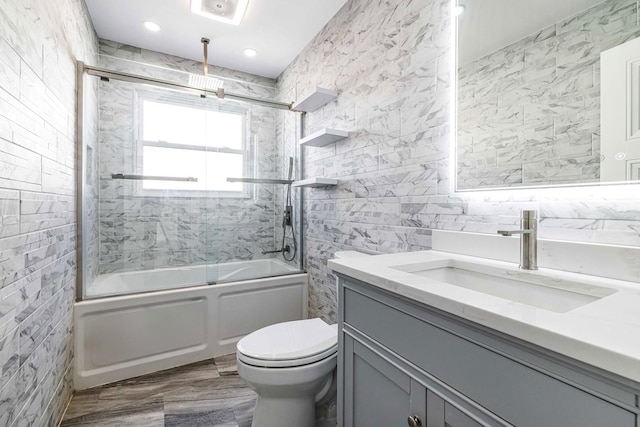 full bathroom with bath / shower combo with glass door, tile walls, vanity, and toilet