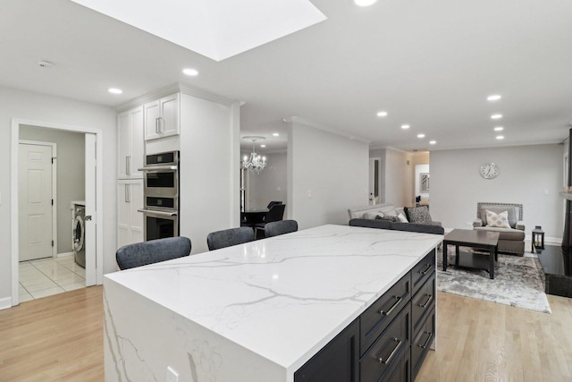 kitchen with washer / clothes dryer, double oven, light hardwood / wood-style flooring, and white cabinets