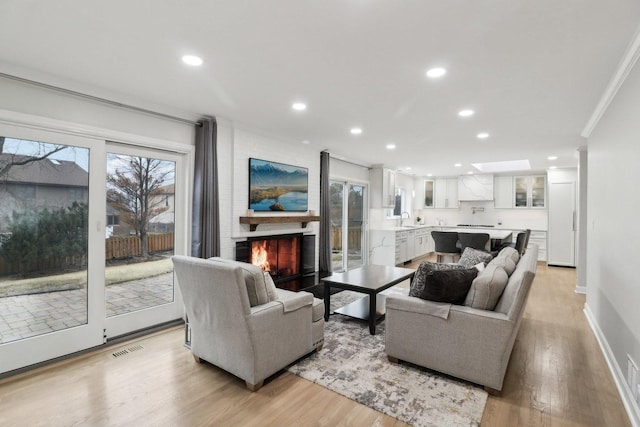 living room with ornamental molding, sink, a large fireplace, and light hardwood / wood-style flooring