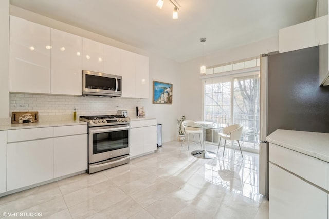 kitchen featuring stainless steel appliances, hanging light fixtures, white cabinets, and backsplash