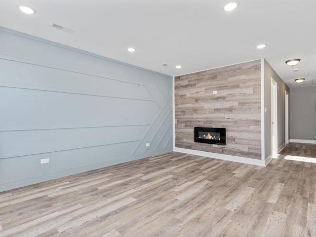 unfurnished living room with a tiled fireplace and light wood-type flooring