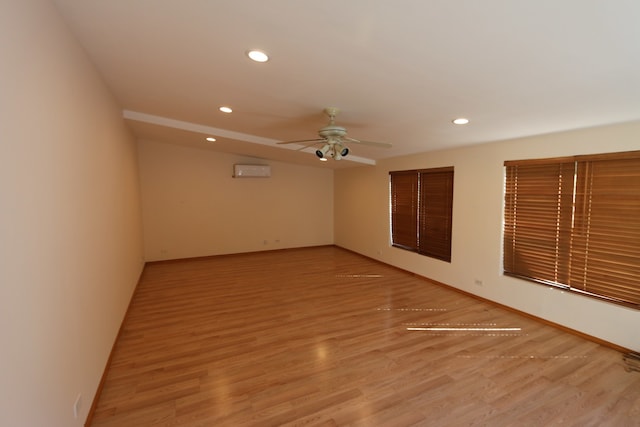 spare room featuring ceiling fan, a wall mounted AC, and light wood-type flooring