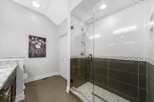 bathroom featuring vaulted ceiling, vanity, an enclosed shower, toilet, and tile patterned floors