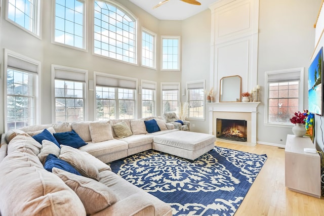 living room with a towering ceiling, light hardwood / wood-style flooring, a large fireplace, and ceiling fan