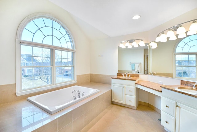 bathroom with a relaxing tiled tub, vanity, vaulted ceiling, and tile patterned flooring