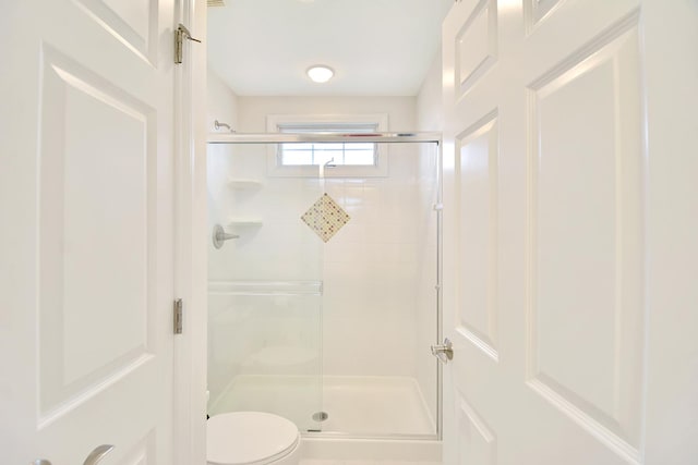 bathroom featuring a shower with door and toilet