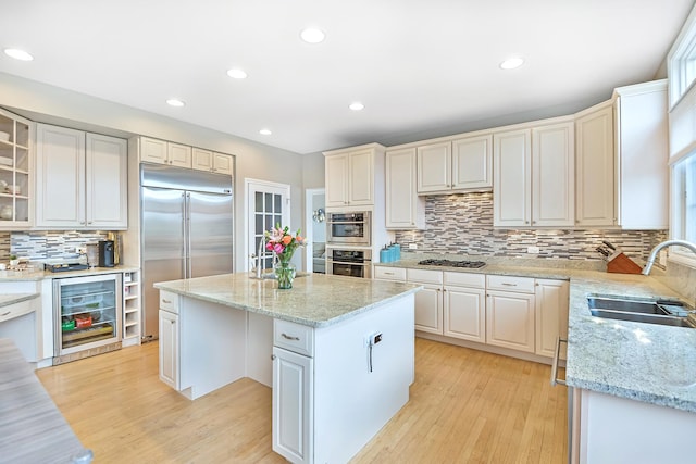 kitchen with sink, stainless steel appliances, a center island, wine cooler, and light stone countertops