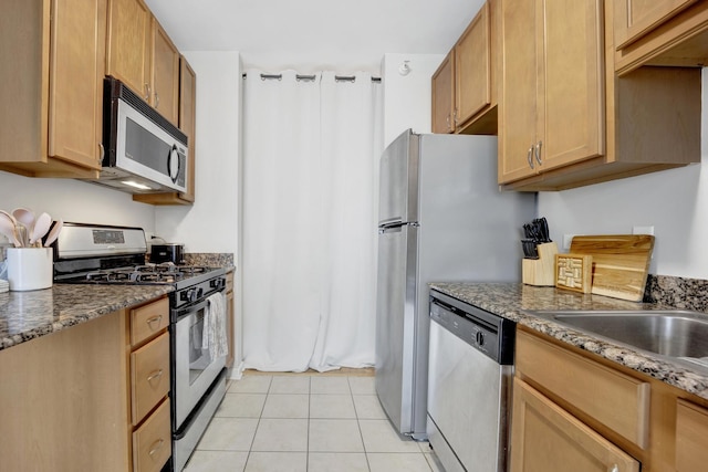 kitchen featuring stainless steel appliances, dark stone countertops, sink, and light tile patterned floors