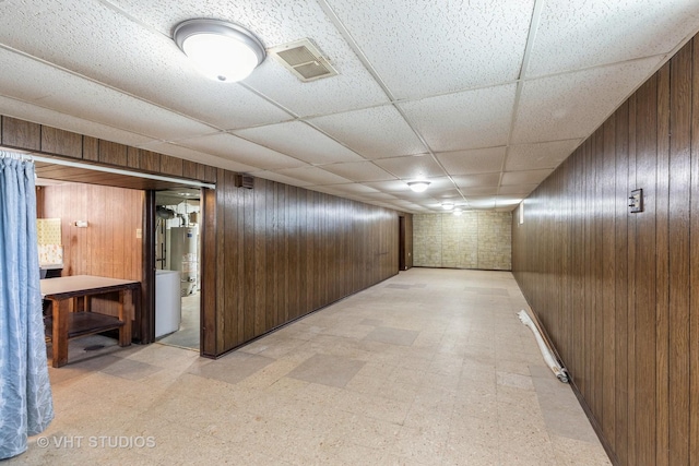 corridor with a drop ceiling, gas water heater, and wood walls