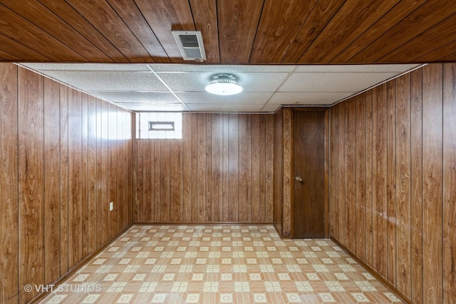 basement featuring a paneled ceiling and wood walls