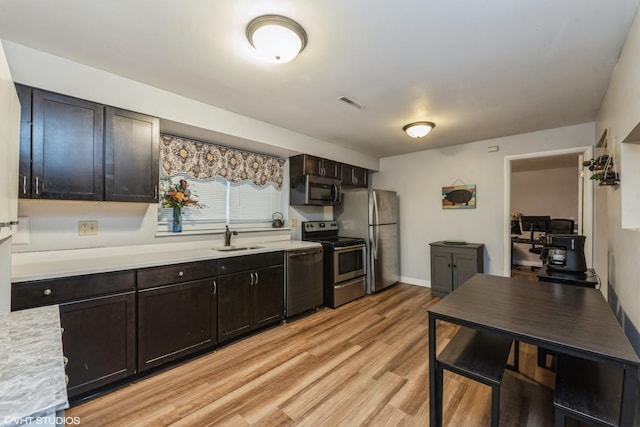 kitchen with dark brown cabinets, appliances with stainless steel finishes, sink, and light hardwood / wood-style flooring