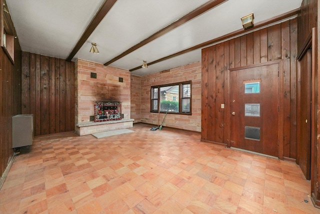 unfurnished living room with a stone fireplace, radiator heating unit, beamed ceiling, and wood walls