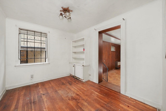 empty room with crown molding, built in shelves, and hardwood / wood-style floors