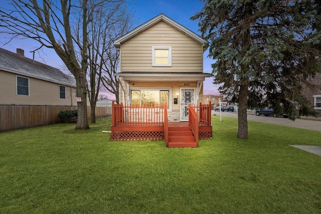 back house at dusk featuring a lawn and a deck