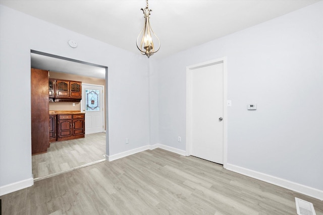 unfurnished room with an inviting chandelier and light wood-type flooring