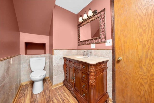 bathroom with vaulted ceiling, tile walls, hardwood / wood-style flooring, vanity, and toilet