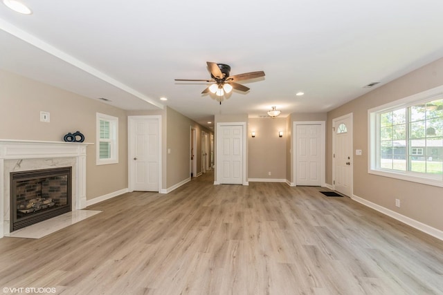 unfurnished living room featuring a premium fireplace, ceiling fan, and light wood-type flooring