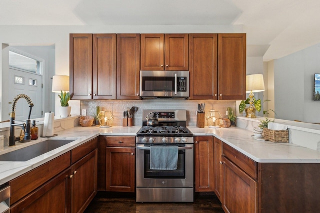 kitchen featuring sink, backsplash, kitchen peninsula, stainless steel appliances, and light stone countertops